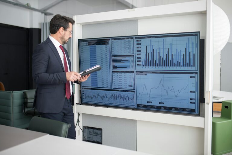 Professional in suit reviews financial charts and graphs on a monitor in a modern office setting.